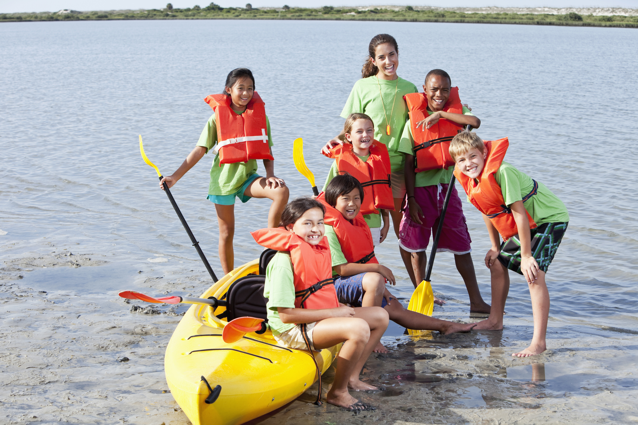 Teenage girl and group of children with kayak at water sports camp.